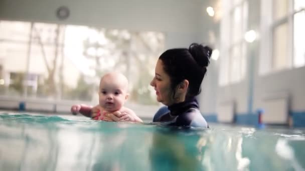 Жінка-тренер або мати вчать маленького малюка пірнати під водою. Він тримає його над водою, а потім пірнає разом під водою. Кадри над і під водою — стокове відео