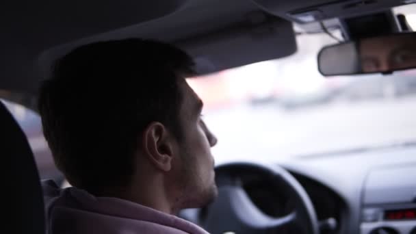 El hombre está conduciendo un coche. Cara de reflexión en espejo retrovisor del vehículo. Hora punta en una ciudad. Filmación del hombro — Vídeo de stock