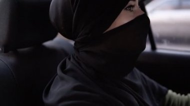 Neşeli, siyah niqab mutlu Müslüman kadın arabada arka koltukta oturuyor, müzik ve dans dinliyor. İyi bir ruh hali. Gündüz. Yavaş çekim