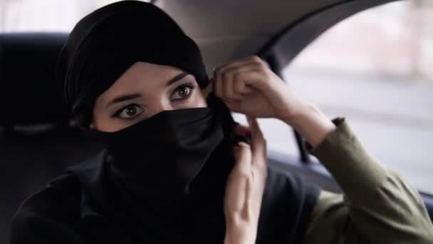 Young woman wearing black niqab. Folowing the rules woman wears the niqab while her road in the car, sitting on a backseat. Slow motion — Stock Video