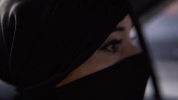Mujer joven vistiendo niqab negro. Siguiendo las reglas de la mujer lleva el niqab mientras su camino en el coche, sentado en un asiento trasero. Cara de cerca — Vídeos de Stock