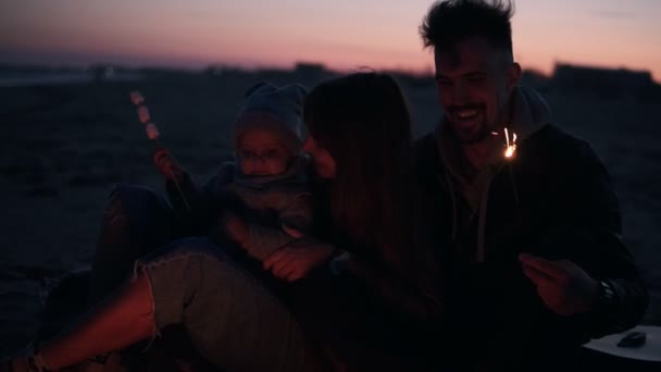 Szczęśliwa, uśmiechnięta rodzina trzech na zewnątrz na plaży siedzi obejmując w pobliżu ognisko z ogumienia, palone marshmallows na patyku. Miłość, happieness i śmiech. Czas wieczorowy — Wideo stockowe