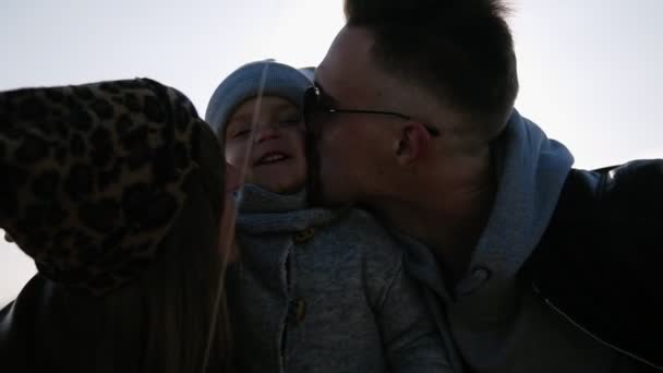 Rodzicielski pocałunek dla dziecka w słońcu, dobry nastrój Młoda para małżeński z synem na otwartym powietrzu, szczęśliwy dziecko stoi obok TOF Mama i tata na zewnątrz, kochający Ojciec i szczęśliwy matka pocałunek małego chłopca. Niski kąt — Wideo stockowe