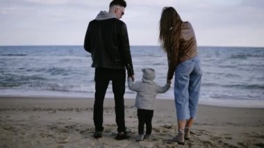 Genç, moda çift güzel sahne çocukları ile denizin önünde duran ve ufukta bakıyor. Rüzgarlı, soğuk hava. Kamera uzaklaşıyor. Nadir görünüm