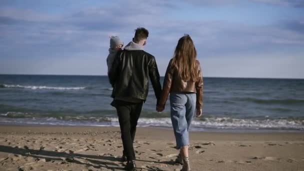 Ung familj, en far med sin son på armarna, promenader längs stranden av svanen, på kusten. En lycklig familj går längs stranden och håller varandra i handen. Sällsynta — Stockvideo