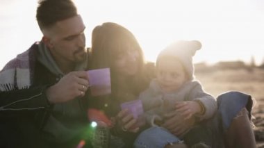 Ekose giyen ve birlikte vakit geçiren, plastik bardaklardan sıcak içecekler içen, rahat giyimli genç şık ailenin güzel sahnesi. Soğuk hava, hafta sonu eğlencesi. Lens üzerinde fişekleri