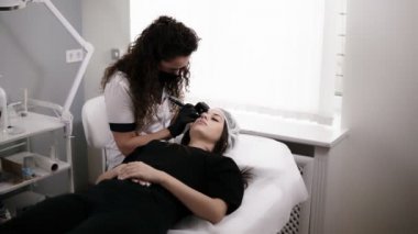 Güzellik uzmanı bir güzellik salonunda bir kadın için iğne ile kaşların şeklini çiziyor veya düzeltme yapıyor. Kalıcı makyaj için profesyonel ekipman. Modern kozmetoloji