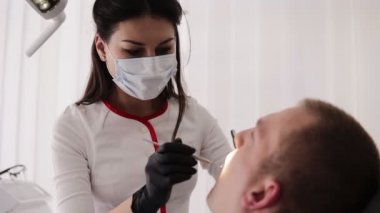 Maskeli kadın diş hekimi hastanın ağız boşluğunu inceler. Adam diş sandalyesinde oturuyor, diş bakımı konsepti. Tedavi sürecinde labcoat ve maske genç diş hekimi. Yakın çekim