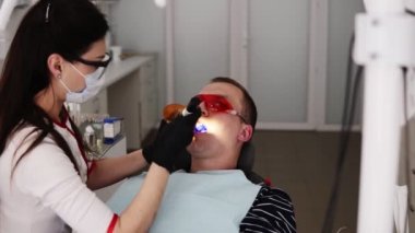 Modern diş ocabinet koruyucu turuncu gözlük kadın doktor ve erkek hasta. Diş hekimi turuncu koruyucu ekran ile dolguların polimerizasyon yapıyor
