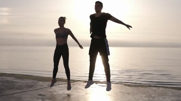 Счастливые мужчины и женщины занимаются профессиональным фитнес-спортом, совершая прыжки с трамплина или приседания, упражнения на открытом воздухе. Медленное движение — стоковое видео