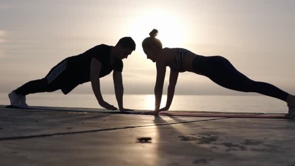 Positivo casal atlético alta cinco vezes durante o exercício fora em frente ao mar. Homem alegre e mulher apto bater palmas enquanto segurando uma prancha e trabalhando na natureza. Parceiros de formação — Vídeo de Stock