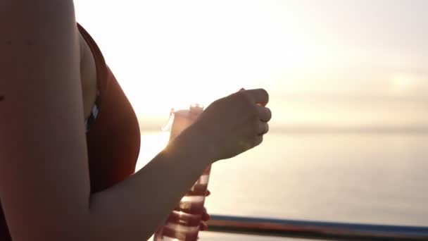 Vista lateral de la hermosa chica en ropa deportiva abre su botella deportiva de color rosa y agua potable después del entrenamiento cerca del mar. Buenos días. — Vídeo de stock