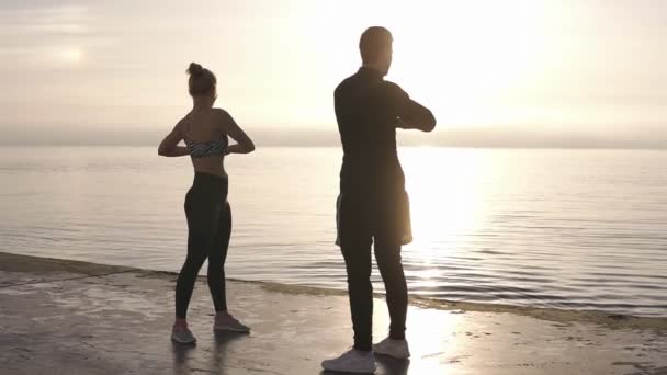 Concept de fitness, de sport, d'entraînement et de style de vie - couple souriant s'étirant à l'extérieur au bord de la mer au lever du soleil matinal. Sport engagé femme et homme exerçant à l'extérieur — Video