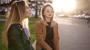 Sokakta birlikte oturan iki kızın yavaş çekim görüntüleri. Girly şeyler, manikür, oje vb tartışıyor Güzel uzun saçlı şık giysiler genç bayanlar. Güneş parlıyor