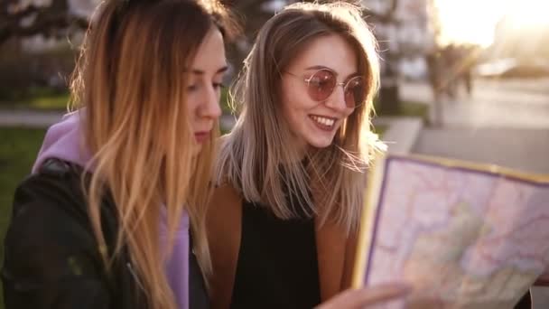 Duas meninas turistas elegantes em roupas casuais de outono, desfrutando de suas aventuras na nova cidade. Guia de viagem, turismo na Europa com amigos.Olhando para o mapa juntos, rindo. Sol brilha no fundo — Vídeo de Stock