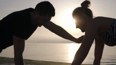 Pozitif atletik omuzlar denizin önünde dışarıda egzersiz. Neşeli adam ve uygun kadın çift bir tahta tutarak ve doğada egzersiz yaparken dokunmadan. Arka planda sabah yumuşak gündoğumu