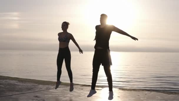 Fitness, deporte, personas, ejercicio y concepto de estilo de vida: hombre y mujer felices dedicados al deporte de fitness profesional haciendo sentadillas de salto o de salto, ejercicio al aire libre — Vídeo de stock