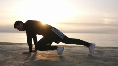 Siyah gömlek ve beyaz spor ayakkabıları içinde Kafkas genç atlet sabah erken denizde deniz kenarında yürüyüş sırasında eğitim süreci. Siyah giyen adam, tahta poz abdominal egzersizleri yapıyor