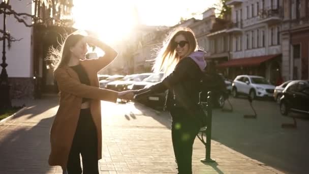 Chicas mejores amigos tomados de la mano y caminando. Vista trasera de dos chicas alegres caminando juntas en el pavimento de la ciudad, burlándose, sonriendo. Conceptos de amistad y estilo de vida. Lente bengalas en el — Vídeos de Stock