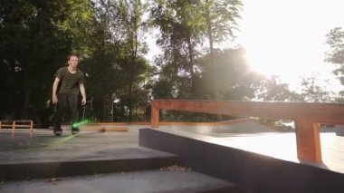 Siyah rahat giysiler genç rulo bir kaykay parkı içinde bir boru ile slaytlar. Genç bir atlet silindirler üzerinde bir hile yapar. Güneşli, yaz günü. Düşük açı görüntüleri