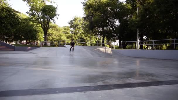 Стройный молодой человек в повседневной одежде катается на роликовых коньках на рампе в скейт-парке, совершает прыжок и зависает в то время. Весна, лето. Медленное движение. Низкий угол съемки — стоковое видео