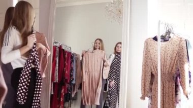 Kız kardeşler veya arkadaşlar giysi butik veya alışveriş merkezi aynabakarken şık elbiseler çalışıyoruz. Satın almak ya da almamak için decising. Ayna yansıma görüntüleri