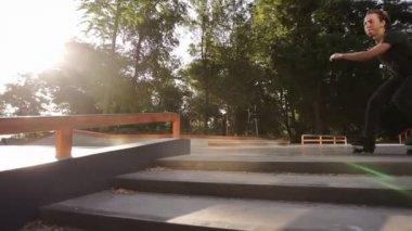 Genç bir atlet silindirler üzerinde bir hile yapar - korkuluklar üzerinden atlar, 360 derece dönüş yapıyor ve havada bacaklarını viraj. Yavaş çekim. Açık paten parkı