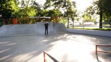 Sıralı patenci rampadan kayan yapıyor ve bir atlama yapıyor, yavaş bir hareketle bacaklar virajlı. Şehir parkında modern paten parkı. Güneşli, yaz günü