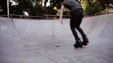 Gündelik kıyafetler giyen bir adam rampadaki paten parkında paten sürüyor. Ağır çekimde bir kaseye binmek. Ekstrem spor, spor eğlence açık havada