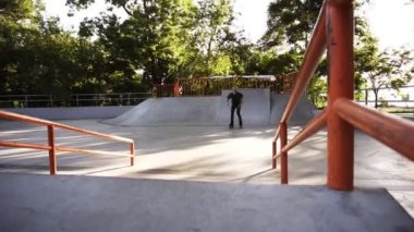 Sıralı patenci rampadan kayan yapıyor ve bir atlama yapıyor, yavaş bir harekette bir bacak virajlı. Şehir parkında modern paten parkı. Güneşli, yaz günü