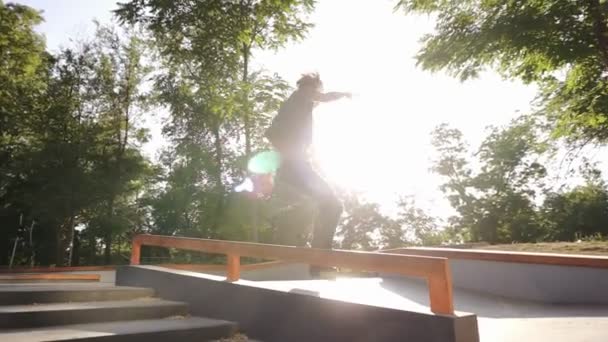 Un giovane atleta esegue un trucco duro sui rulli salta attraverso le ringhiere, facendo doppio giro toe loop, ma fallisce e cade a terra. Al rallentatore. All'aperto skate park — Video Stock