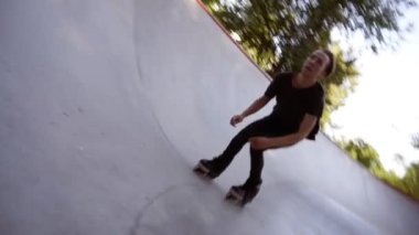 Gündelik kıyafetler giyen bir adamın yakın çekimi rampadaki bir paten parkında paten sürüyor. Yavaş çekimde paten sürmek. Ekstrem spor, spor eğlence açık havada