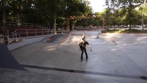 Joven esbelto en ropa casual montando en patines en línea en la rampa en el parque público de patinaje, hace un salto y cuelga en un tiempo. Primavera, hora de verano. Movimiento lento — Vídeos de Stock