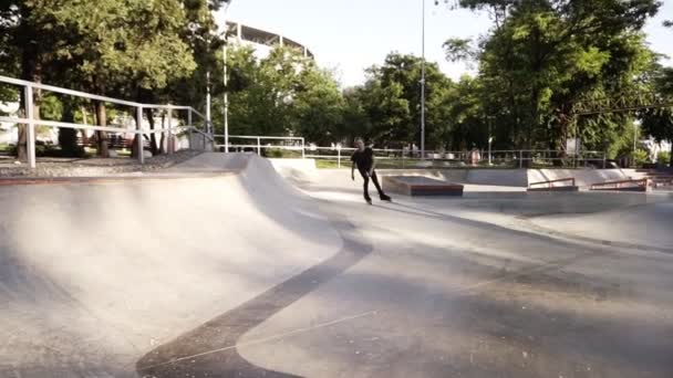 Встроенный роликовый фигурист делает трюки в бетонном скейтпарке на открытом воздухе с красивым зеленым фоном парка, замедленная съемка. Запись крупным планом на верхней части пандуса — стоковое видео