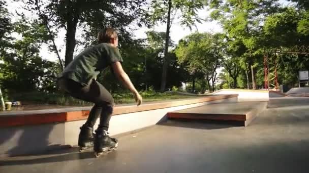 Inseguimento di filmati di un giovane pattinatore che scivola su una ringhiera di legno nel mordern skate park con rampe. Soleggiato, giorno d'estate. Al rallentatore. Da vicino. — Video Stock