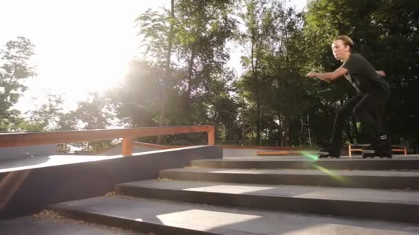 Un joven atleta realiza un truco duro en los rodillos salta a través de las barandillas, haciendo doble vuelta en el dedo del pie y doblar las piernas en el aire. En cámara lenta. Parque de skate al aire libre — Vídeos de Stock