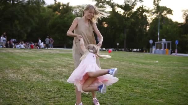 Madre cariñosa caucásica en vestido beige con su pequeña hija divirtiéndose y jugando en el parque. Mamá haciendo girar a su hija, que feliz y riendo en publicidad, parque verde — Vídeo de stock
