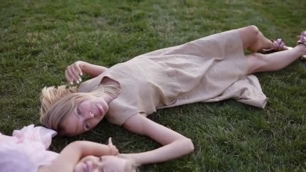 Jeune femme blonde gracieuse avec sa petite fille blonde, se détendre sur l'herbe dans le parc. La mère embrasse son bébé et la regarde avec joie et amour. Vue grand angle — Video