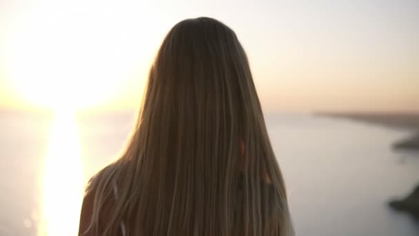 Fechar visão traseira da mulher cabelo claro movimento concurso no ar em câmera lenta. Mulher loira caminhando pelo penhasco. Tocando seu cabelo longo brilhando ao sol no por do sol. Bela natureza — Vídeo de Stock