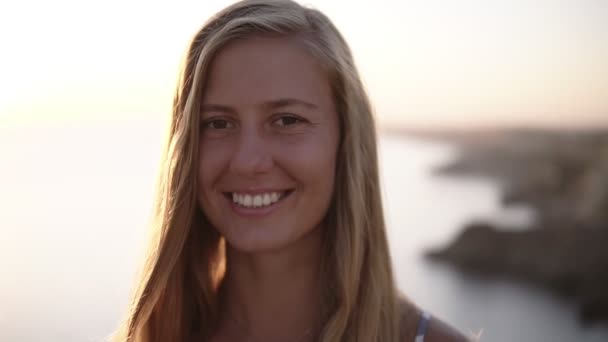 Pretty long haired blonde woman looking straight to the camera and smiling, a little shy. Beautiful nature blurred background — Stock Video