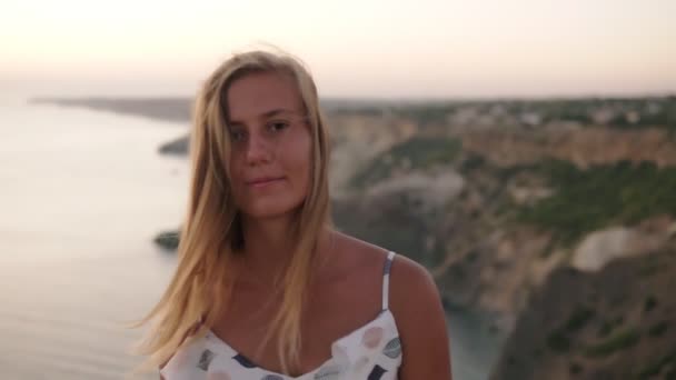 Sunny, long haired blonde woman moving straight to the camera and smiling. Beautiful seaside on the background — Stock Video
