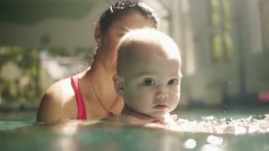 Mutlu beyaz anne ve onun bebek oğlu kapalı yüzme havuzunda yüzme, su altında onu sallayarak. Yüzme havuzuna ilk kez gelen çocuk. Yavaş çekim
