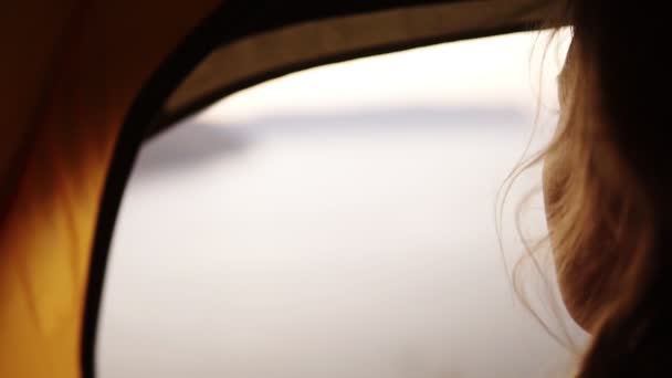 Blurred view of a females face admiring the view of the water- sea or lake from her hiking tent. Sea on the background. Footage from the shoulder — Stock Video