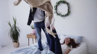 Genç mutlu sevgi dolu çift evde eğlenmek, yatakta ayakta dans, bir ekose ile onları kapsayan gülümseyen kadın, yatak odasında öpüşme birbirlerini kucaklayan hafta sonu harcama
