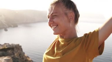 Sarı tişörtlü kadın kampçının portresi ellerini yayıp sabah güneşini karşılıyor. Sabah güneş ışığına karşı bir tepede ayakta, uyandım. Arka planda deniz kenarı ve dağlar