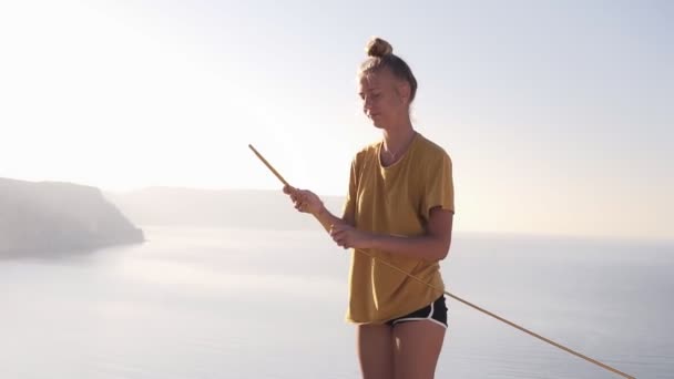 その少女はキャンプの後にテントを分解する。黄色いTシャツを着た観光客の女の子がテントを取り除き、野生のキャンプ。海の近くの崖の上の女性白人女性。スローモーション — ストック動画