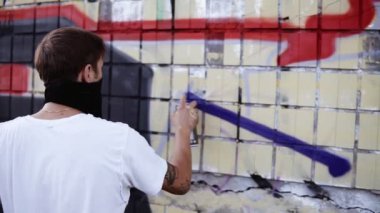 Bir çalışma sürecinde genç adamın yakın çekim sprey bir sokak bina duvarına mavi renkli bir çizgi çizim uygulayarak. Resim oluşturma. Grafiti oluşturma sürecinde sokak sanatçısı. Arka görünüm
