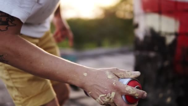 Primo piano di artisti mano scuotendo l'aerosol e iniziare ad applicare vernice spray. Azione. Le dita macchiate di artista tengono bomboletta spray con vernice colorata su muro di cemento. Artista di strada in procinto di — Video Stock