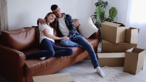 Das junge Paar ist müde, nachdem es sein neues Haus bezogen hat und sich auf dem Sofa ausgeruht hat. Mädchen stützt sich auf ihren Freund, atmet aus — Stockvideo