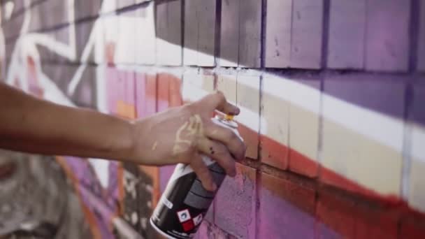 Close-up van kunstenaars hand vuil in verf aanbrengen spray tekening een wit gekleurde lijn op een straat gebouw muur. Actie. Gekleurde vingers van kunstenaar vasthouden spuitbus met gekleurde verf op betonnen muur — Stockvideo